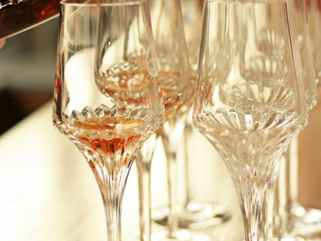 Two rows of empty wine glasses and a bottle of liqueur being poured into one glass.