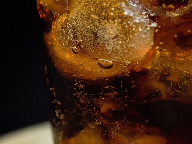 Fizzy brown soda or tea in a clear glass with ice cubes and citrus wedge