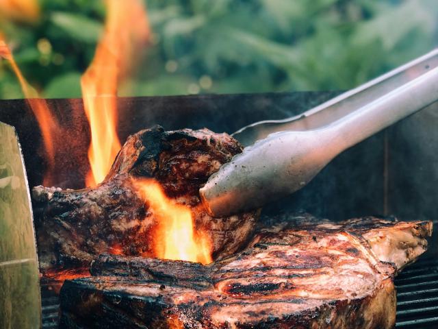 a grill with flames and tongs turning some charred meat.
