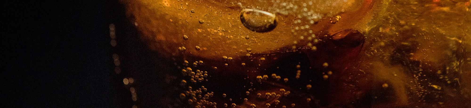Fizzy brown soda or tea in a clear glass with ice cubes and citrus wedge
