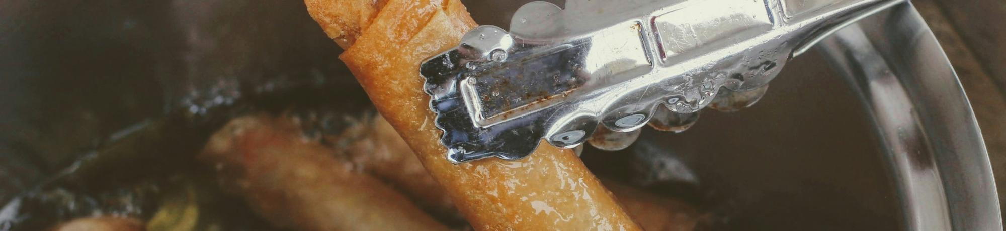 Cooking tongs holding fried spring rolls over boiling oil in a pot 